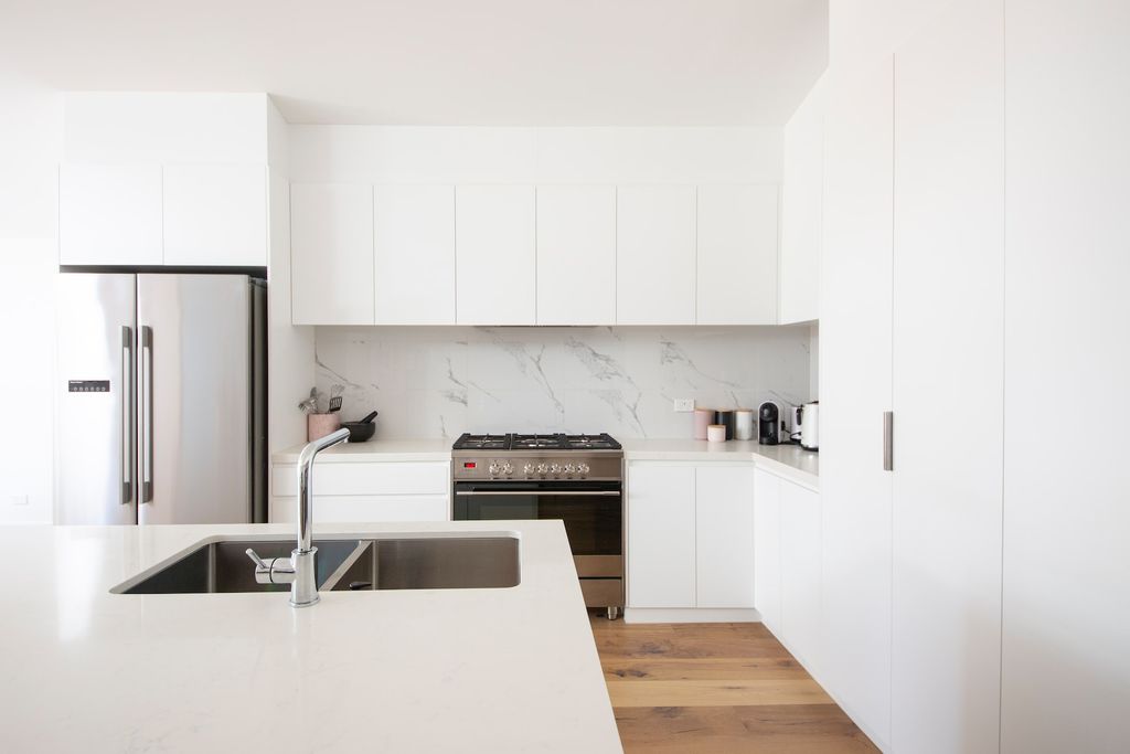 White kitchen cabinets with white countertops, stainless steel appliance and wood floors
