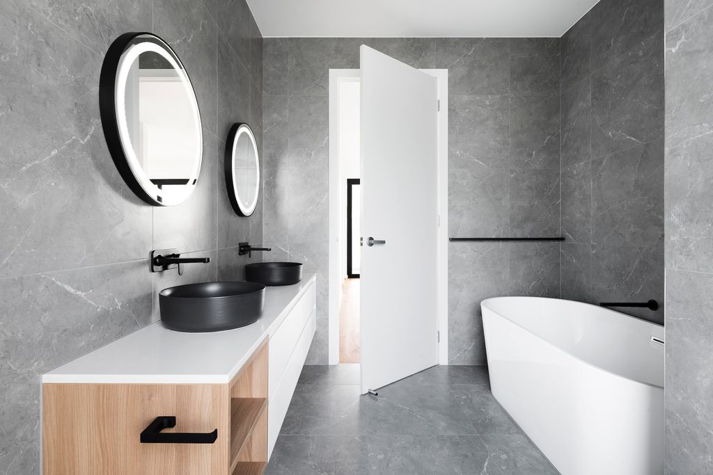 Bathroom with large grey times, black double sinks and white tub