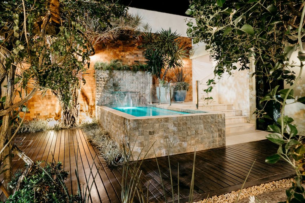 Patio with greenery, wooden deck and stone pool