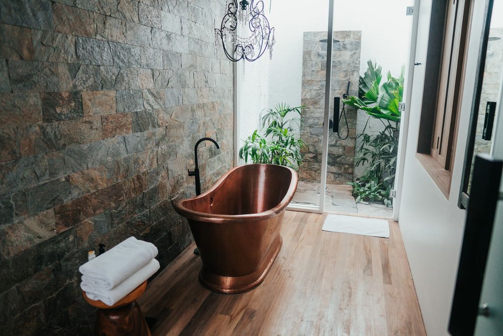 Bathroom with stone wall, wooden floors and copper freestanding bathtub