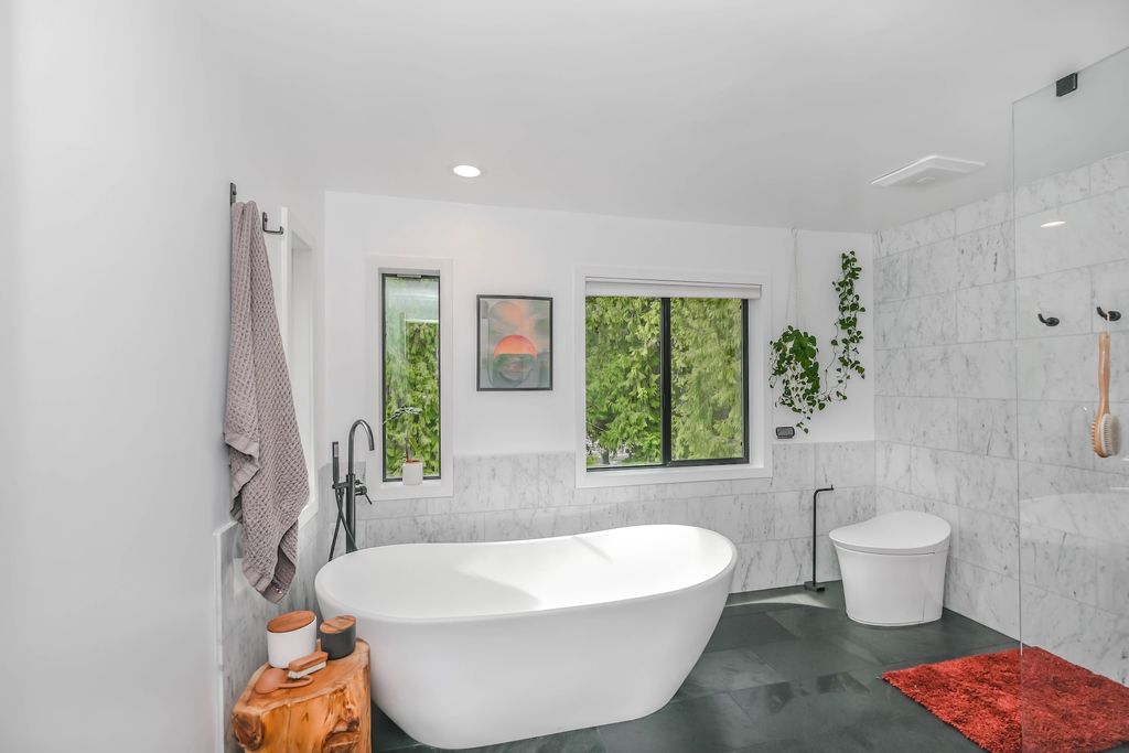 Bathroom with white bathtub and toilet, dark grey floor tiles and windows