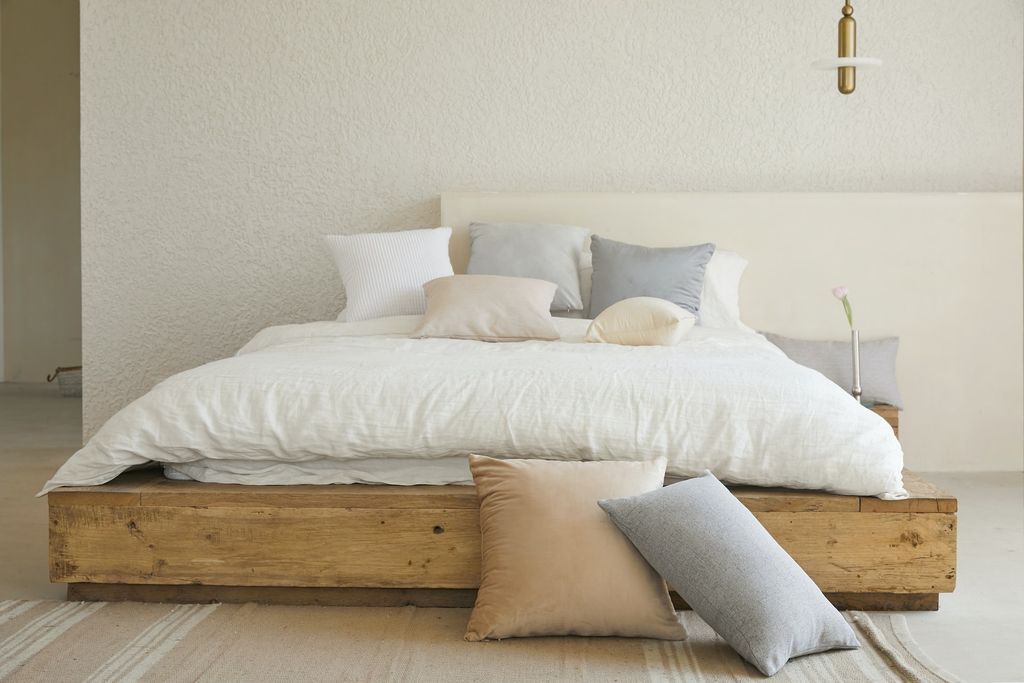 Wooden bed with white sheets and nude coloured pillows